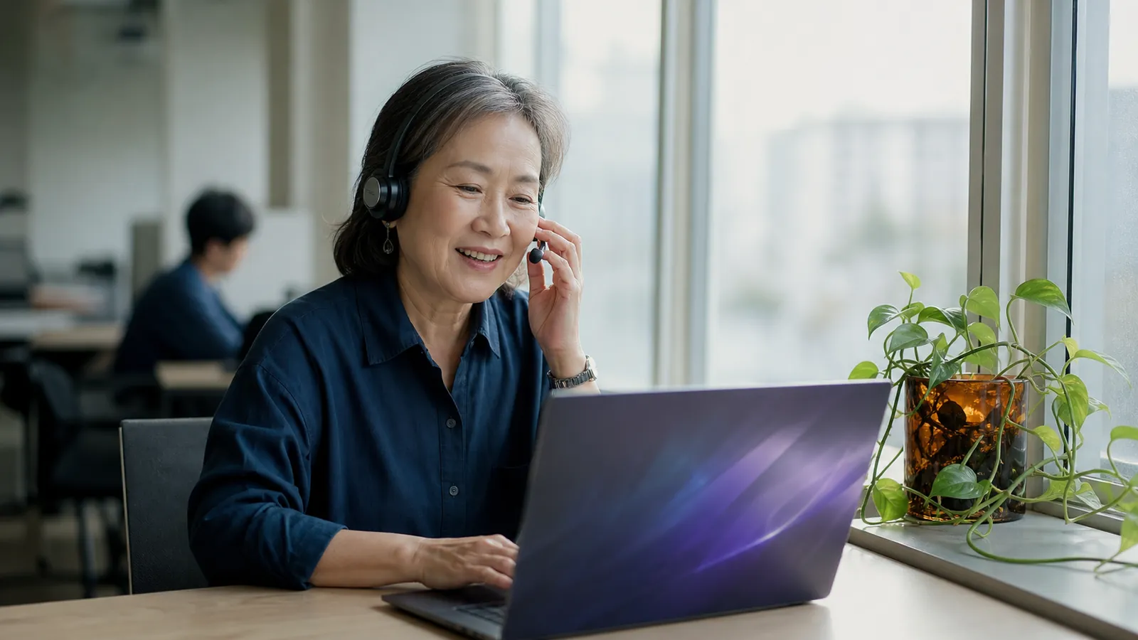Operations director relaxed on a routine call at a window desk, one laptop glowing softly